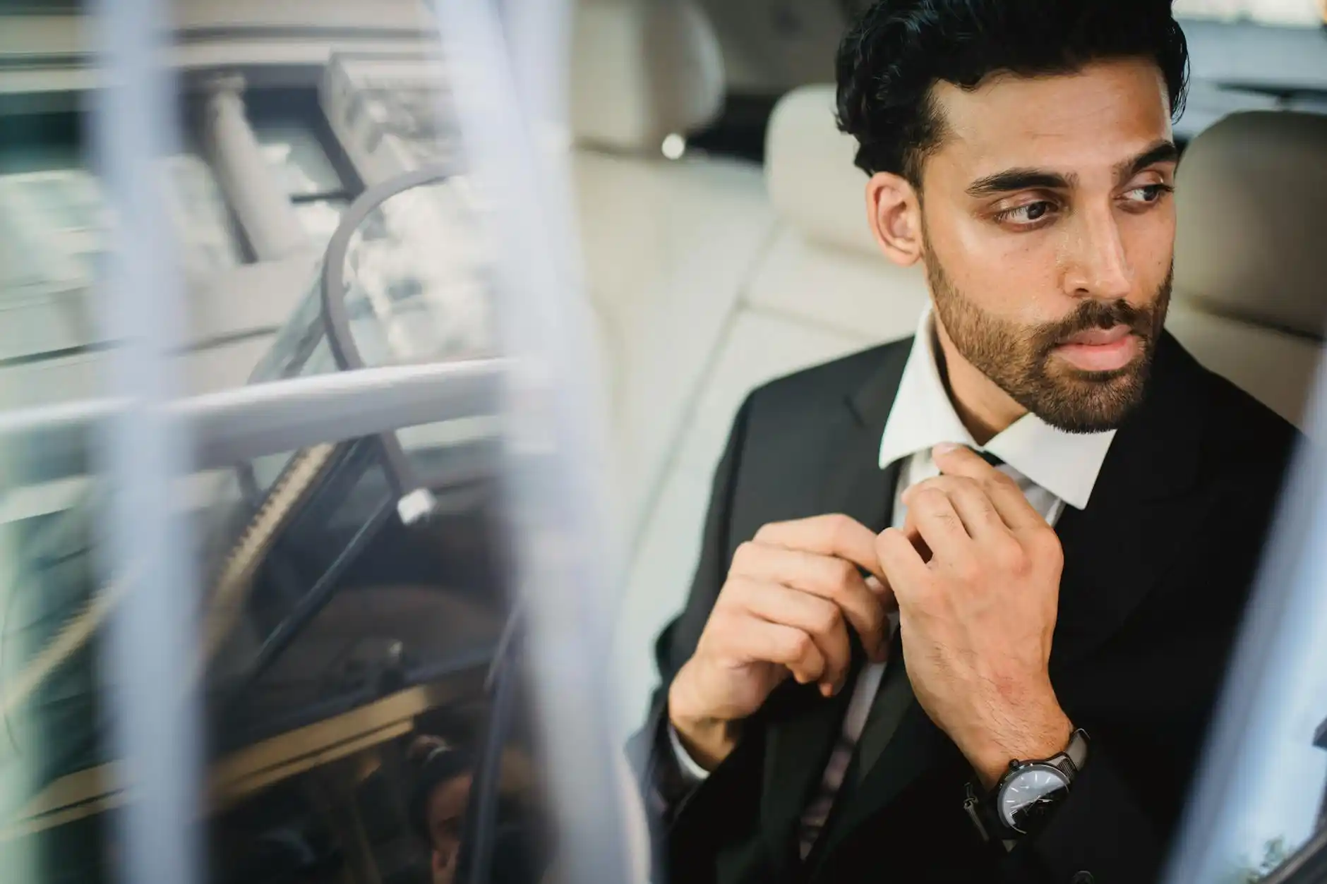 chauffeur in dark suit checking flight status on a tablet beside a polished black town car, Seattle skyline faintly visible in the background at dawn