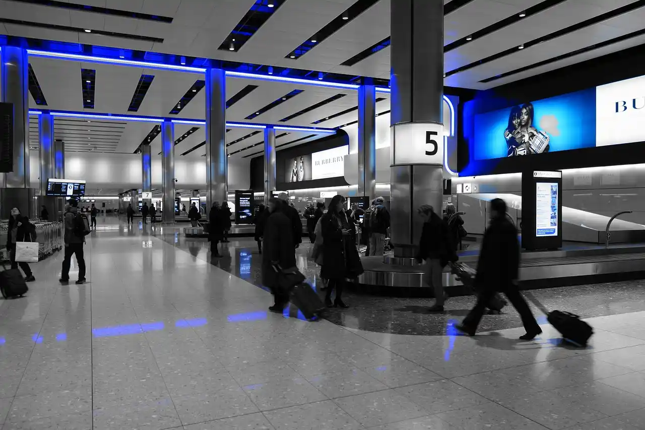 chauffeur in black suit holding a digital name sign inside Sea-Tac baggage claim, arriving passenger smiling beside stacked suitcases, bright airport lighting and directional si...