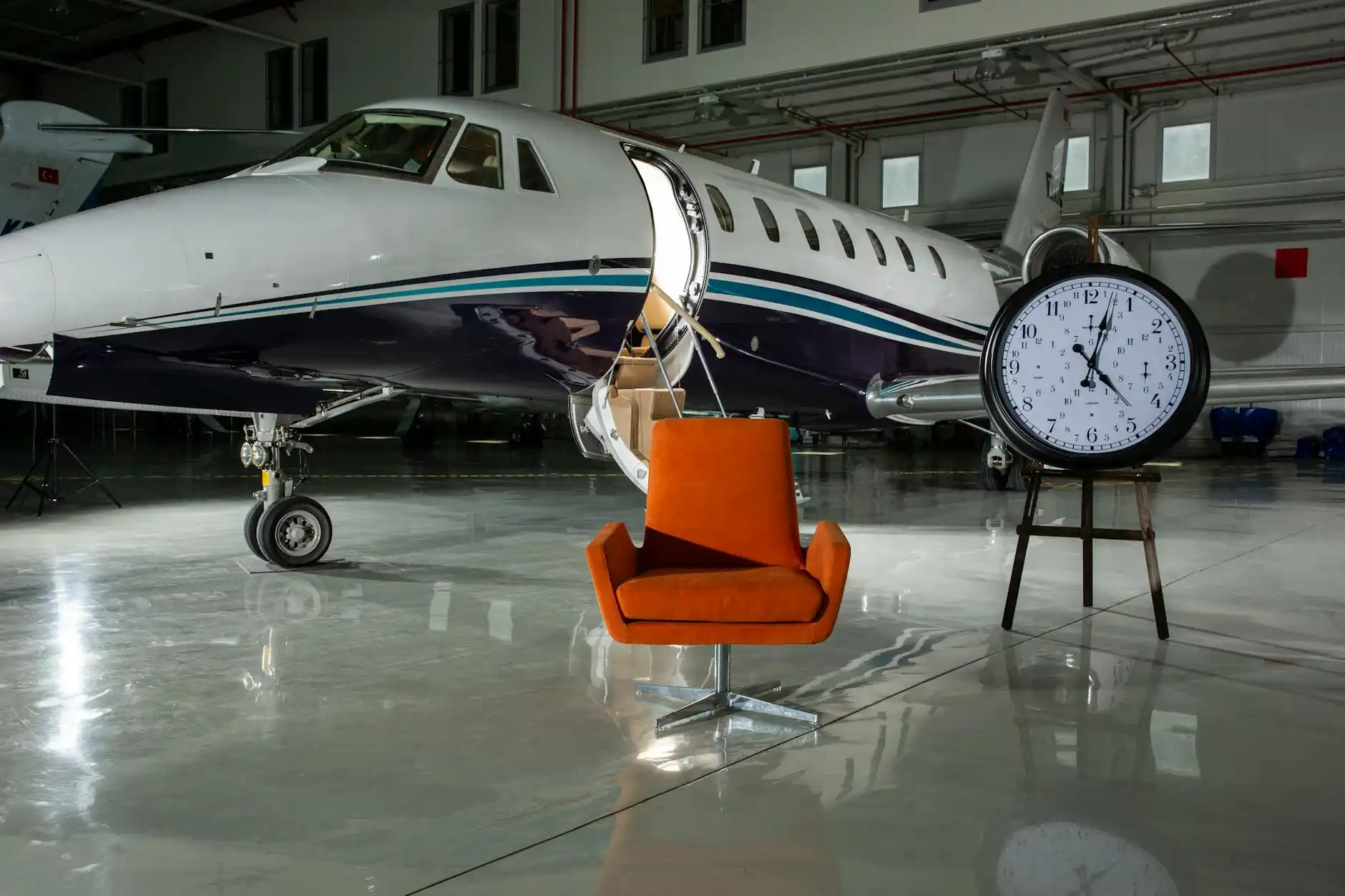 professional chauffeur in dark suit holding a tablet with passenger name inside a modern FBO lounge at Boeing Field, with leather seating, espresso bar, and jet visible through ...