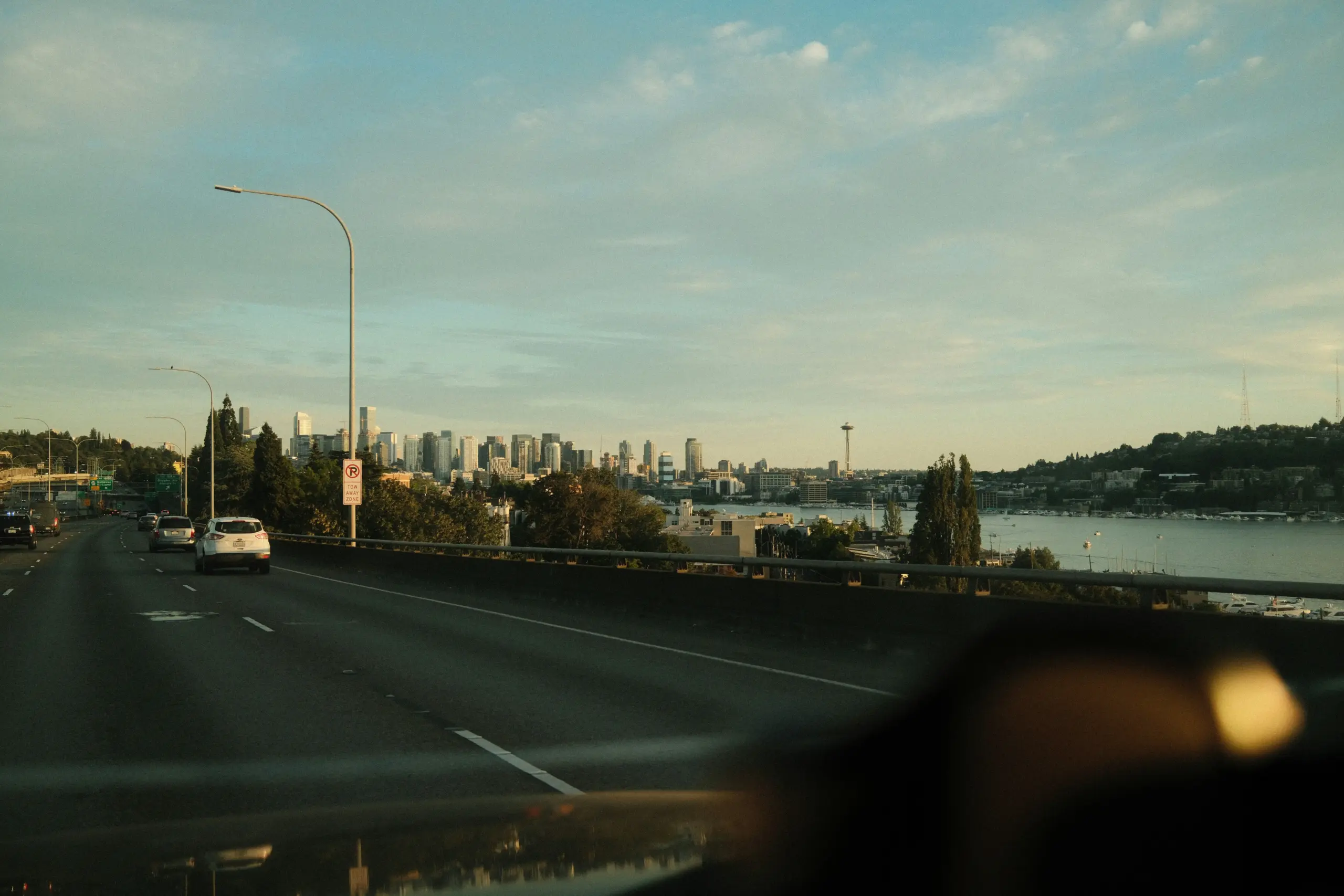 professional chauffeur in a polished black luxury sedan parked curbside in downtown Seattle, rainy street reflections, modern office towers, discreet executive passenger enterin...