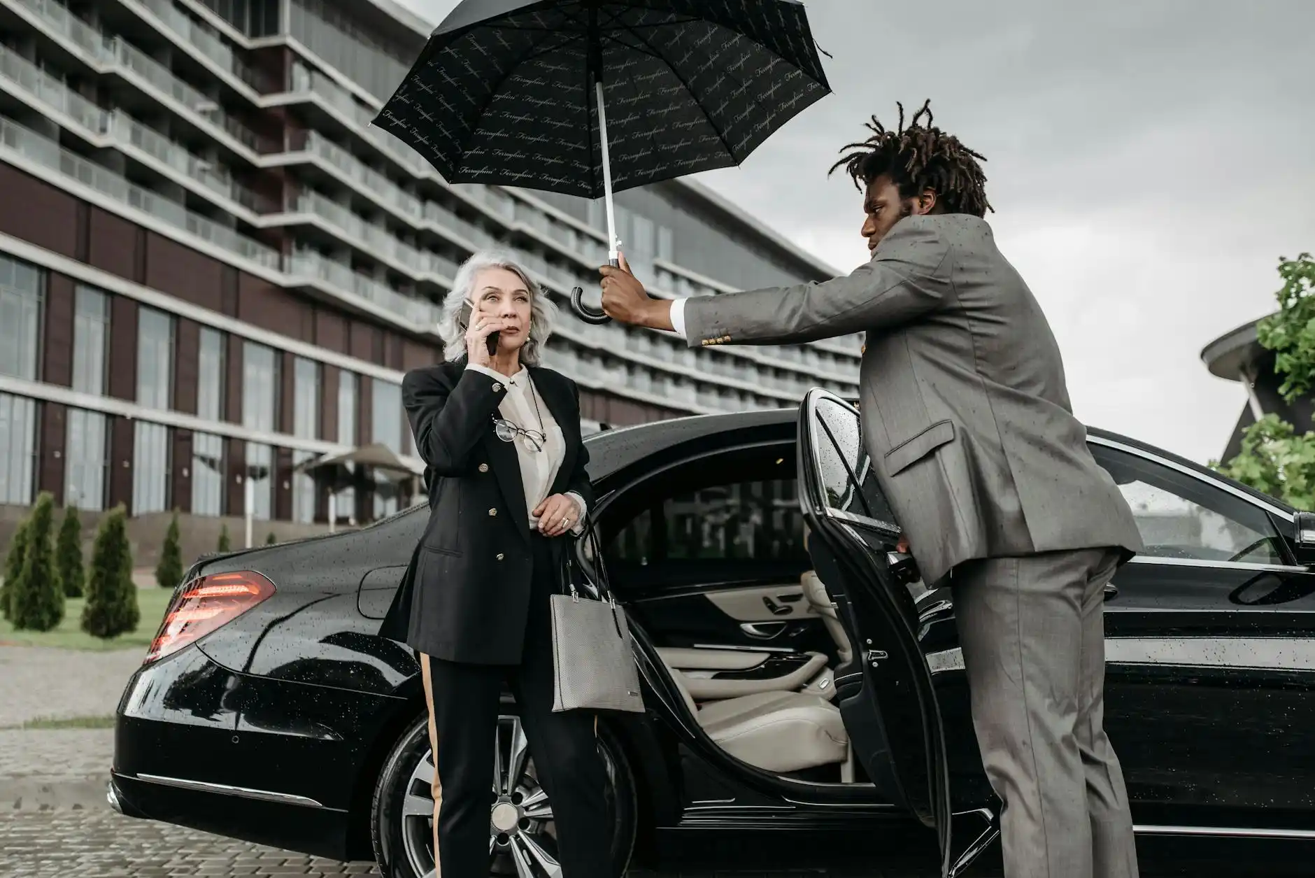 elegant chauffeur in dark suit holding umbrella for executive client outside a luxury hotel in Seattle, valet entrance, glass facade, soft overcast light