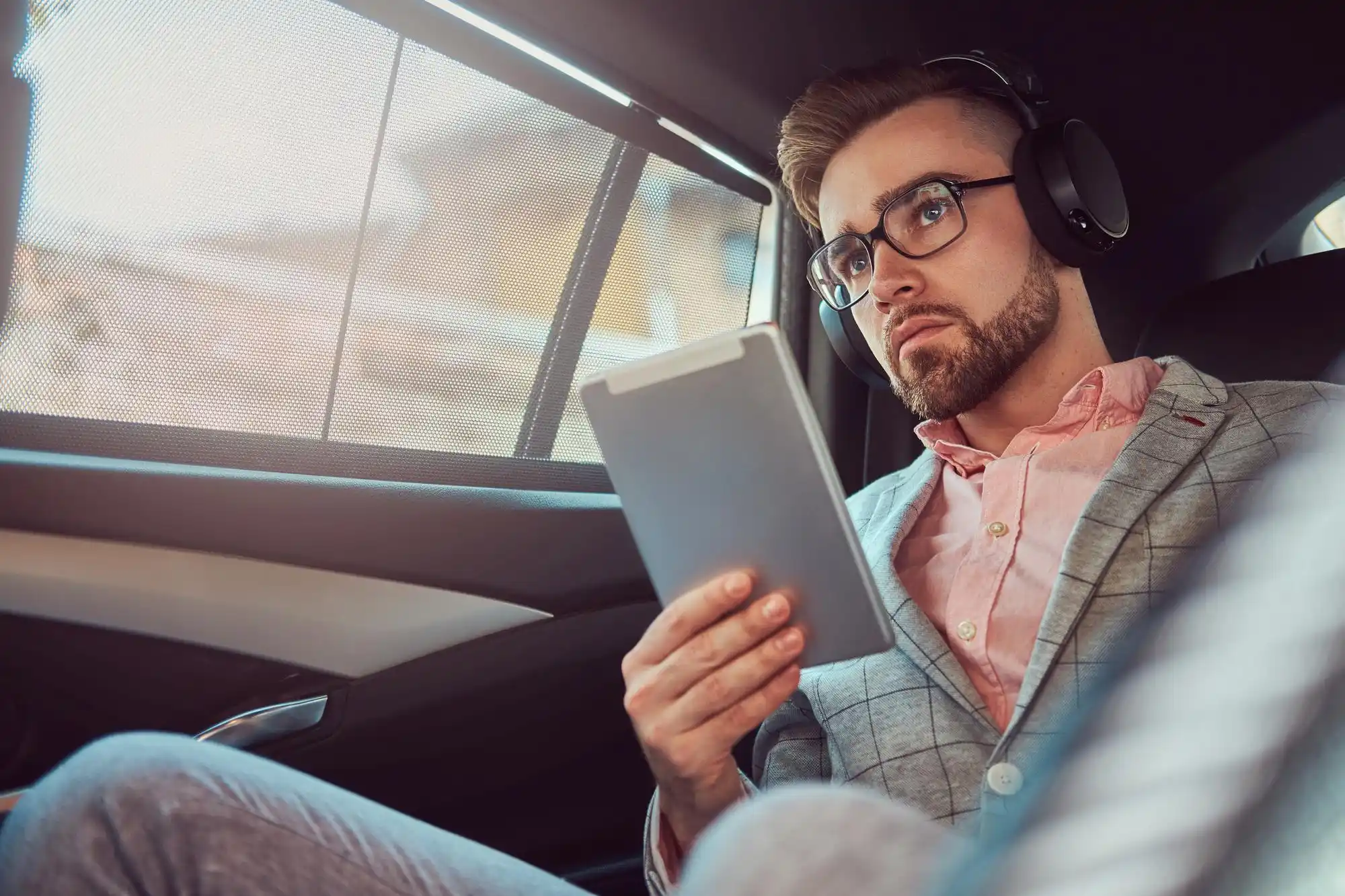 Seattle executive seated in rear of luxury sedan reviewing presentation on tablet, city skyline and Space Needle visible through rain-speckled window, refined corporate atmosphere