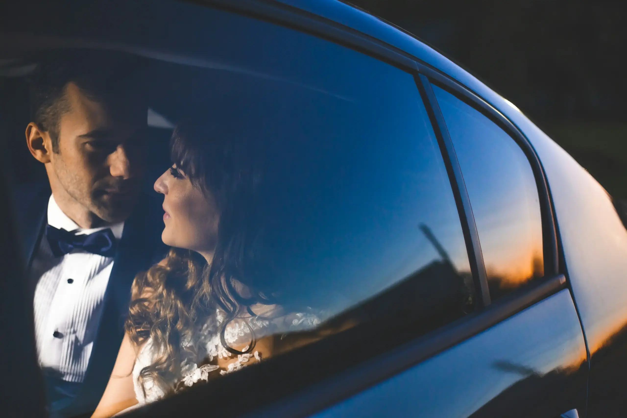 chauffeur opening the rear door of a luxury town car for a smiling couple dressed for an anniversary, Pike Place Market and Seattle waterfront softly visible in the background