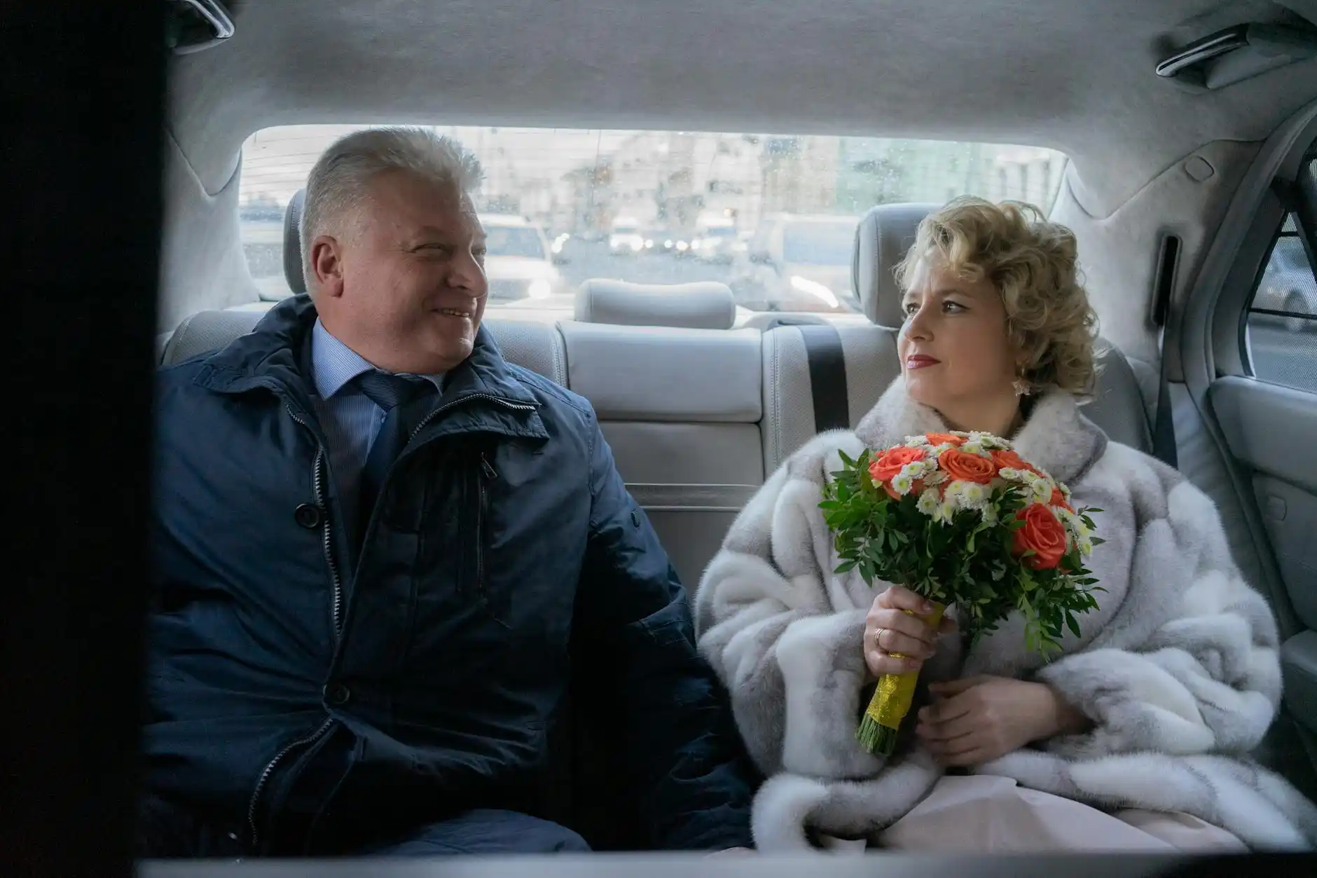 elegant couple inside a luxury car with soft ambient lighting, bouquet of flowers on the seat, Seattle theater district outside the window, rain-speckled glass