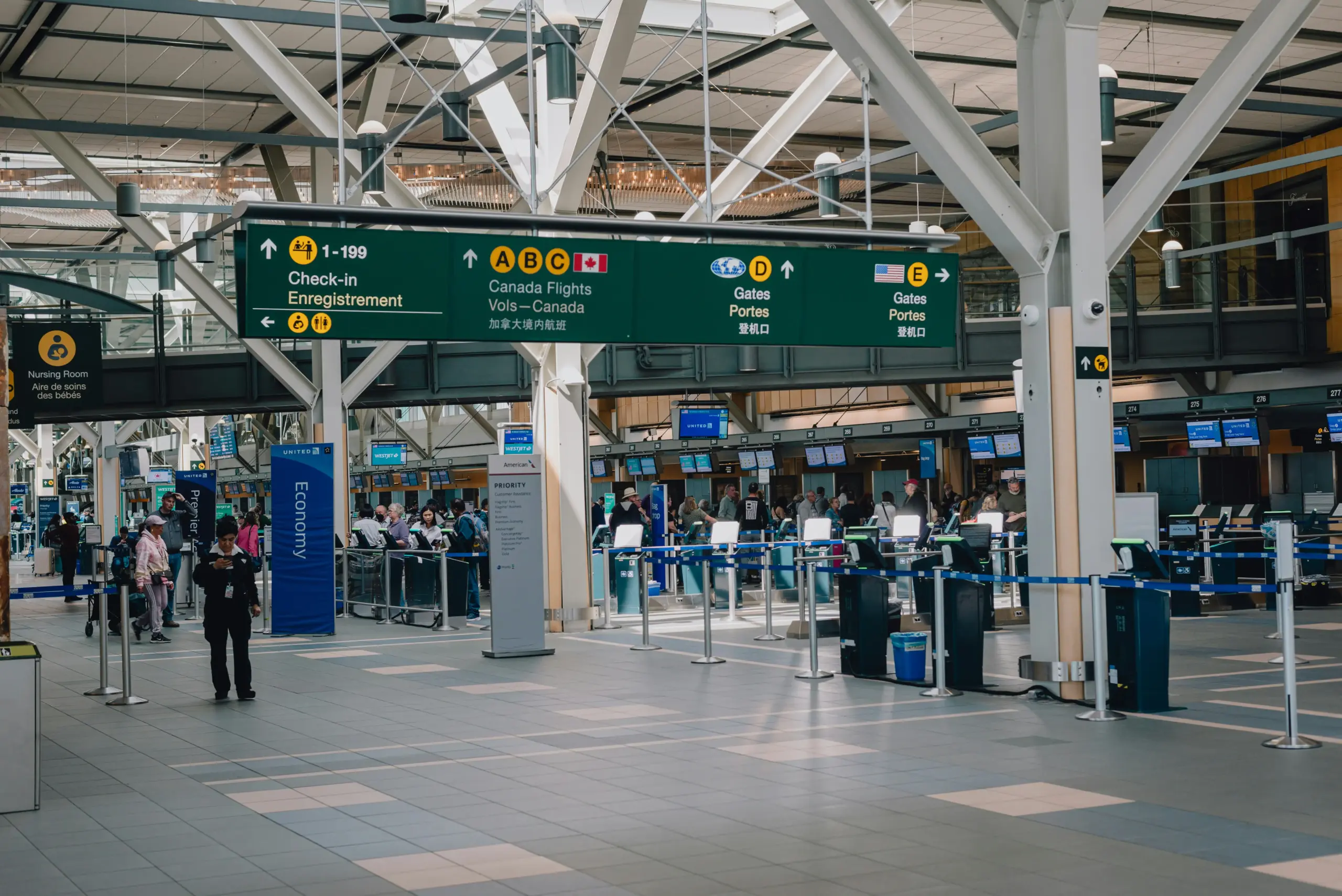 airport arrivals board showing delayed and updated flights beside chauffeur checking phone in terminal pickup area with polished black suitcase