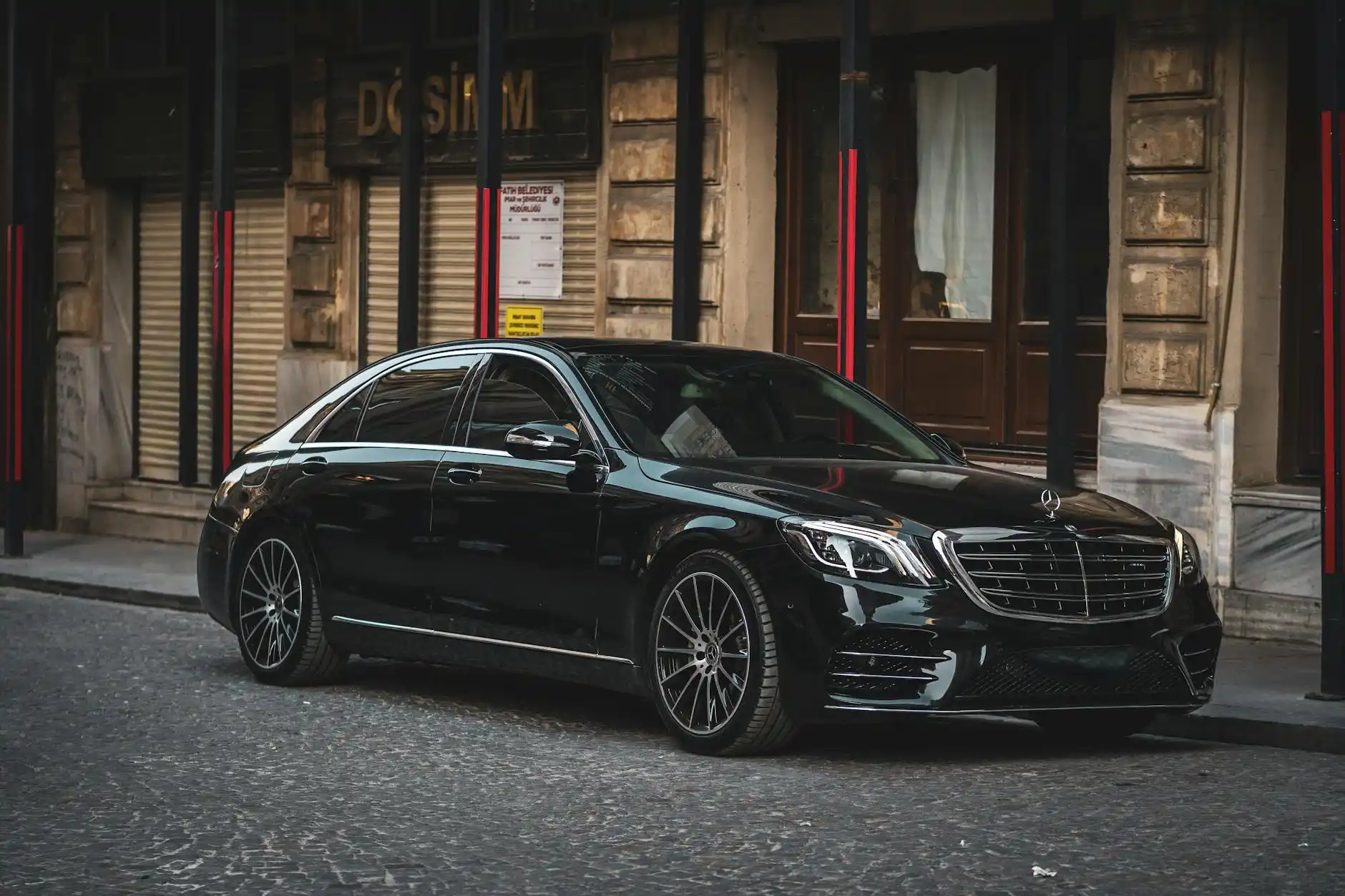 professional black luxury sedan parked at SeaTac Airport curbside at sunrise, chauffeur in dark suit opening rear passenger door, travelers with rolling luggage, modern terminal...