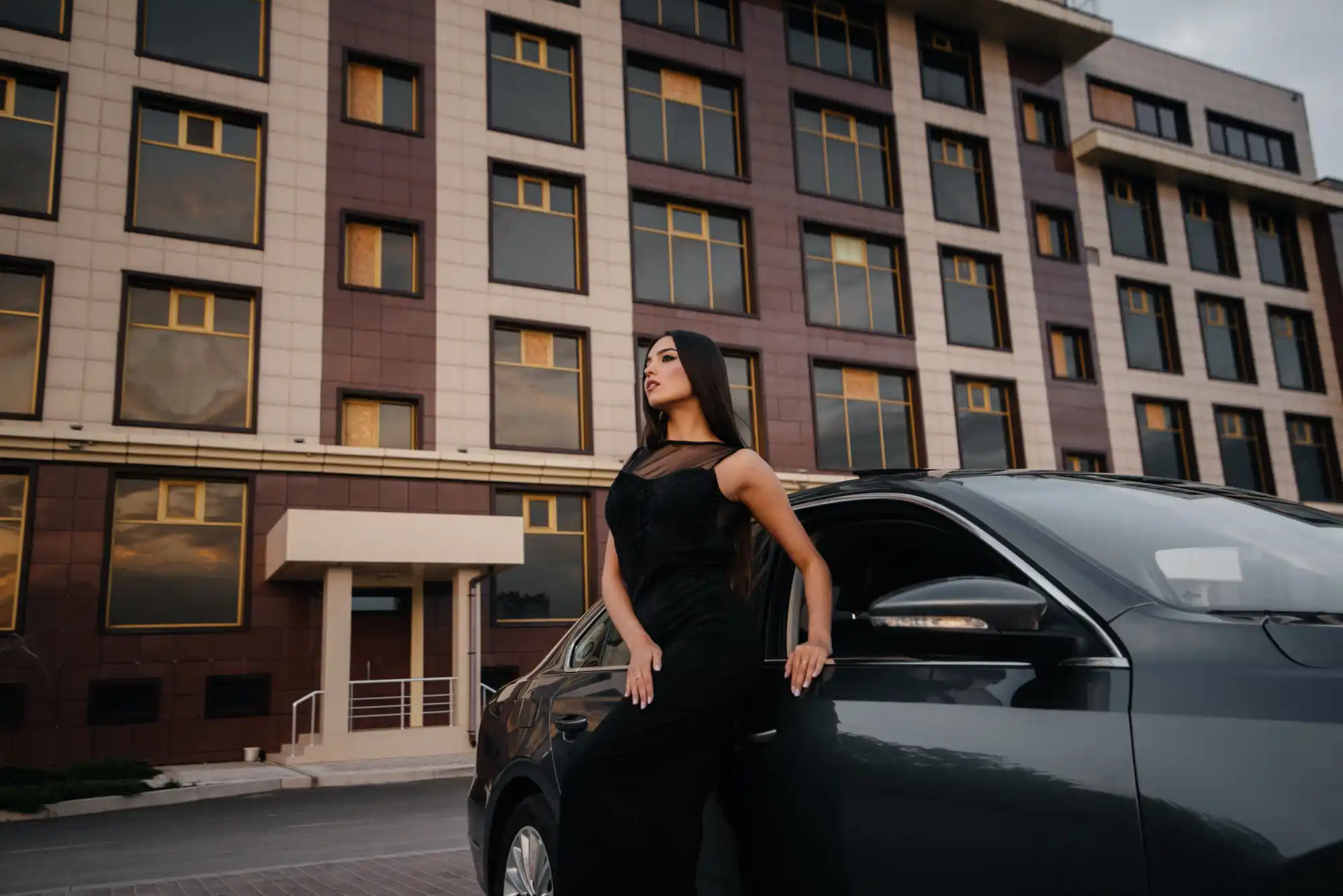 diverse group of travelers including business executive, family with children, and older couple beside a sleek black town car outside a contemporary Seattle hotel entrance