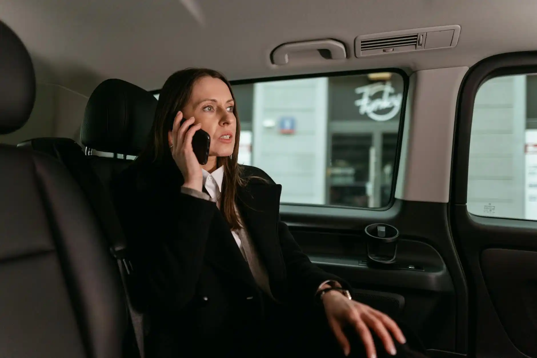 close-up of a professional chauffeur in dark suit and tie checking reservation details on a tablet beside a polished black town car at Sea-Tac Airport arrivals