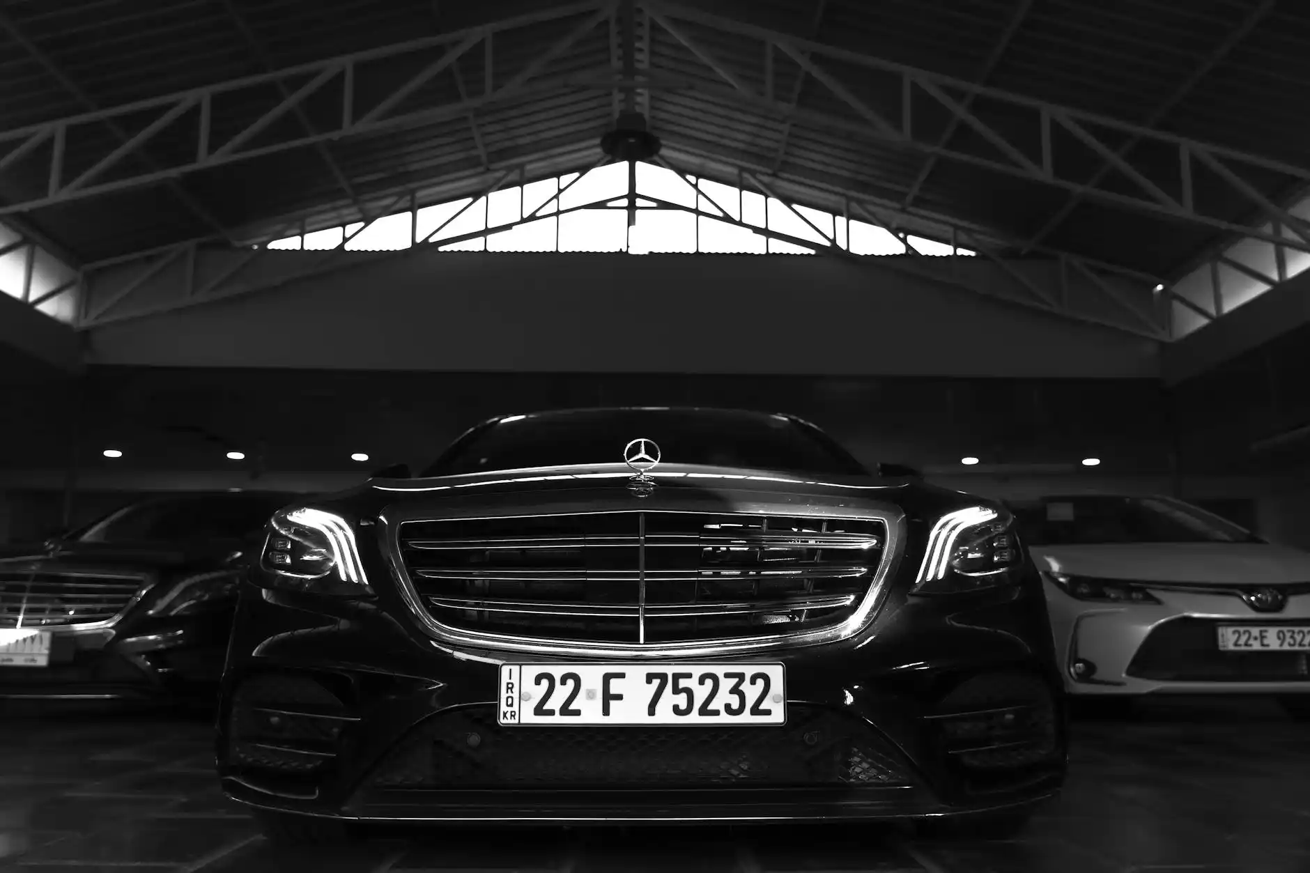 nighttime Sea-Tac Airport curbside pickup with a polished black sedan under airport lights, chauffeur holding a tablet with passenger name, rain reflections on the pavement and ...