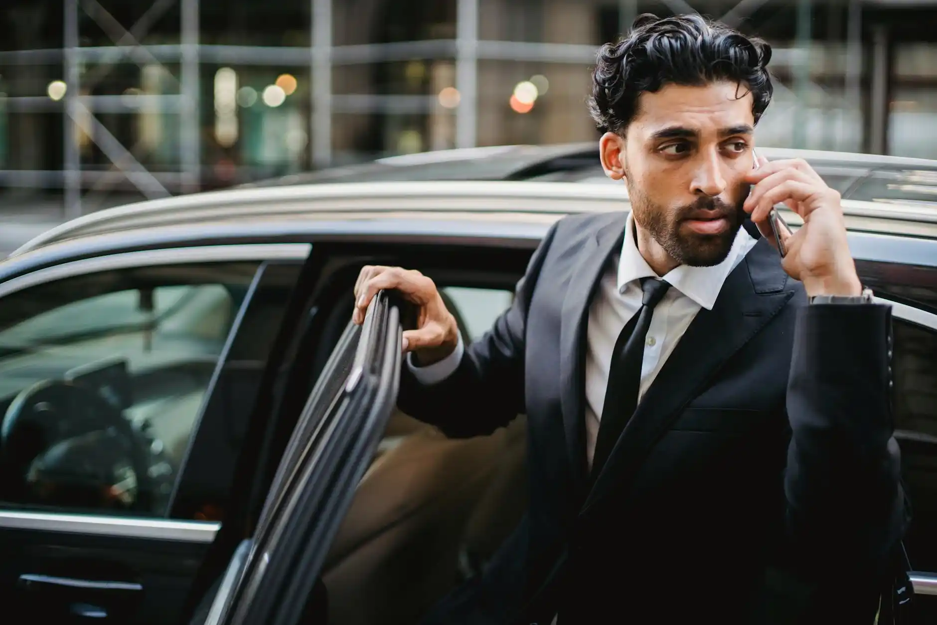 discreet executive arrival scene at a luxury downtown Seattle hotel entrance, black town car parked curbside, suited chauffeur standing professionally, executive stepping out wh...