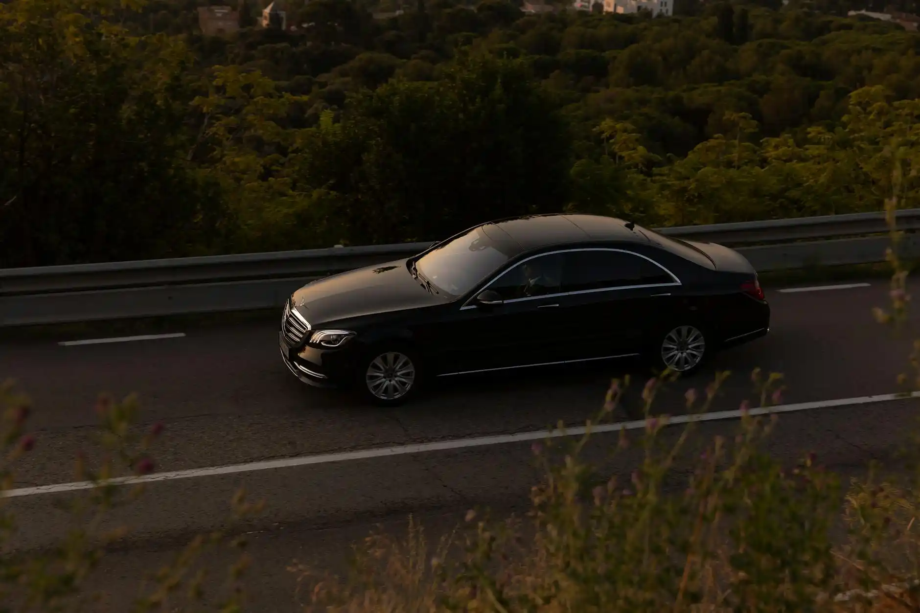 black luxury sedan arriving at Seattle-Tacoma International Airport curbside at sunrise, professional chauffeur opening rear door, rolling luggage, soft golden light reflecting ...