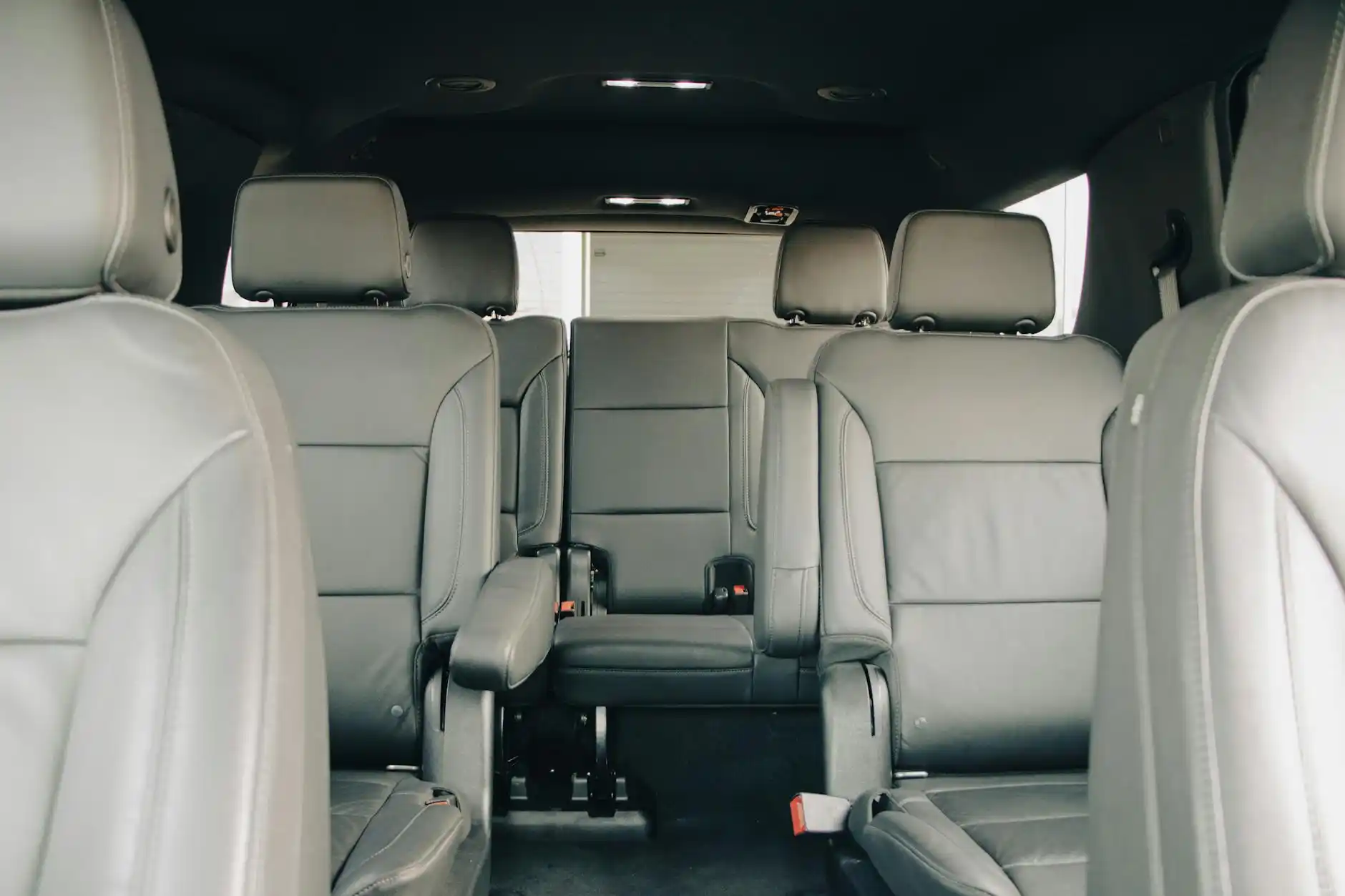 professionally dressed executive travelers seated inside a luxury SUV with tan leather interior, laptops and carry-on luggage visible, Seattle skyline through rain-speckled windows