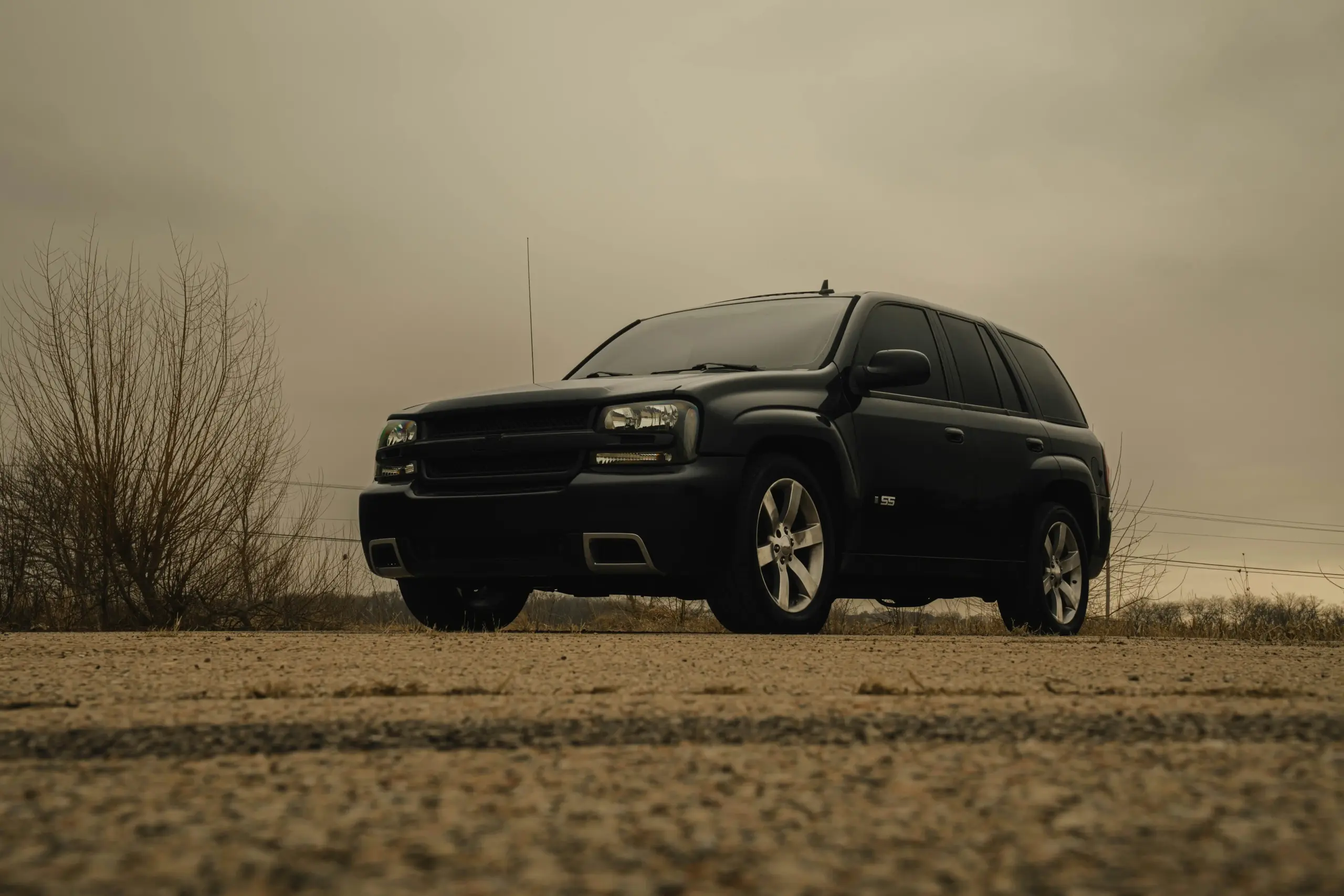 black luxury SUV arriving at Seattle-Tacoma International Airport curbside on a rainy evening, glossy paint reflecting terminal lights, professional chauffeur opening rear passe...