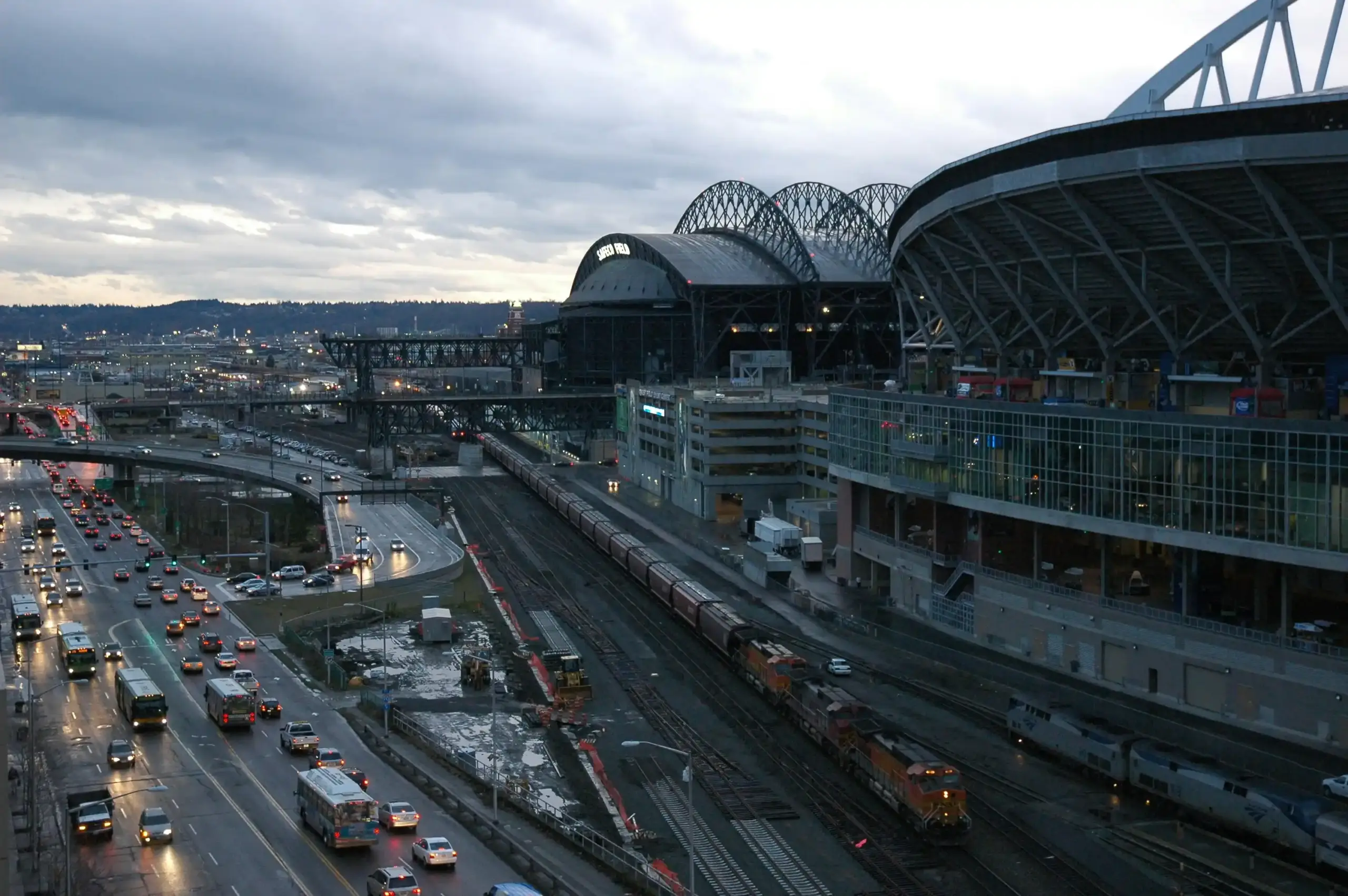 black luxury limousine pulling up to Seattle-Tacoma International Airport arrivals curb on a rainy evening, glowing terminal lights reflecting on wet pavement, chauffeur opening...