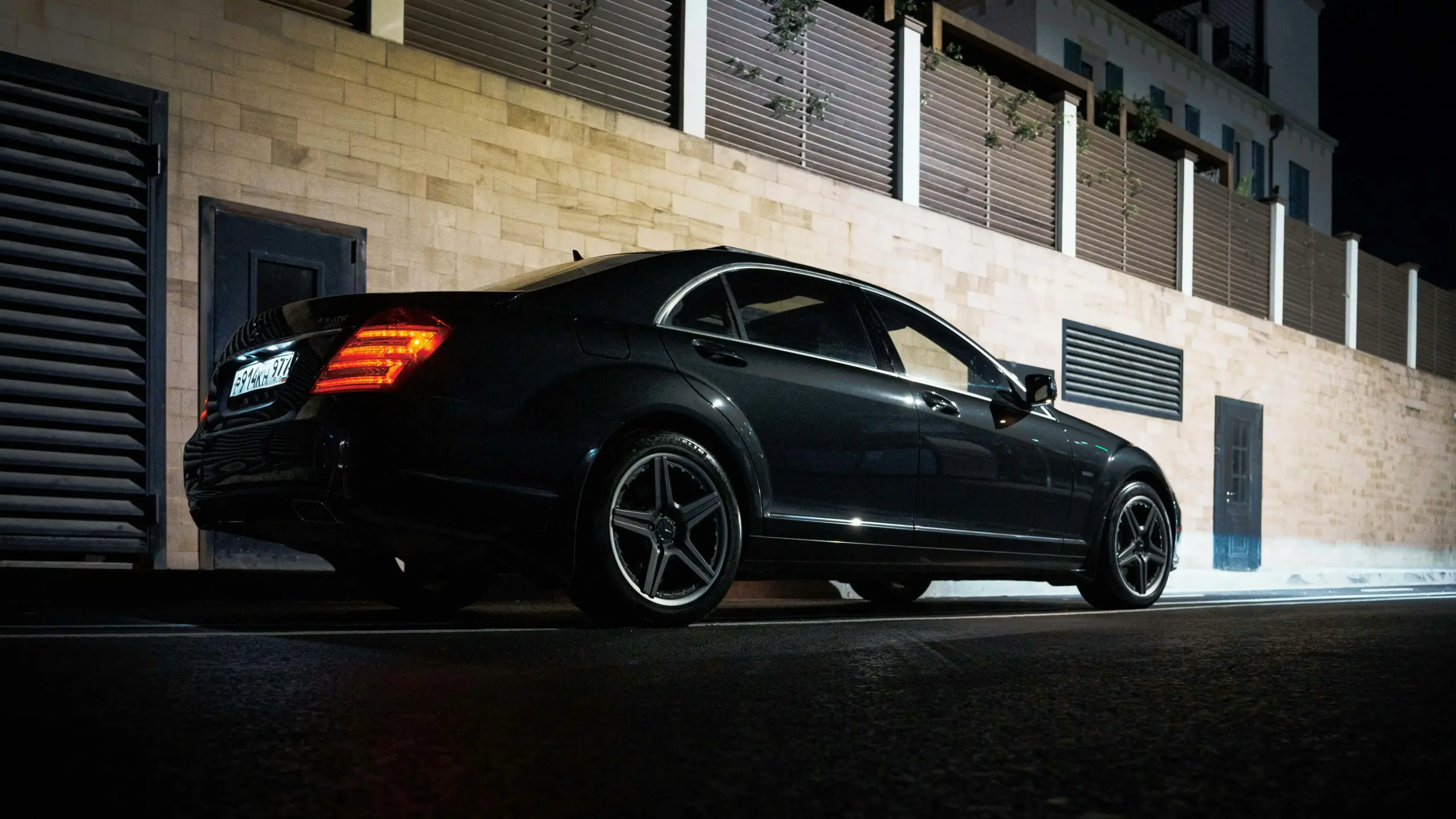 black luxury sedan arriving at an upscale Seattle restaurant entrance at dusk, executives in business attire stepping out, downtown lights reflecting on wet pavement, valet staf...