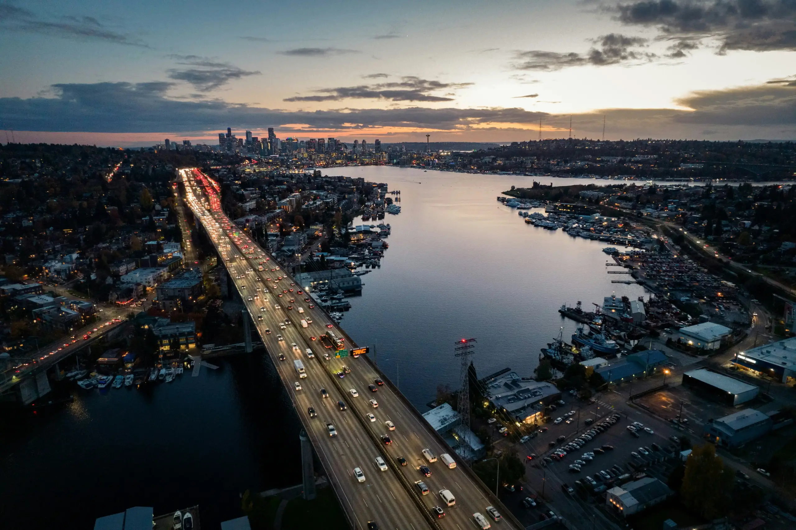 aerial evening view of downtown Seattle streets with traffic, glowing restaurant signs, valet stand, and a chauffeured black SUV pulling up near a high-end steakhouse