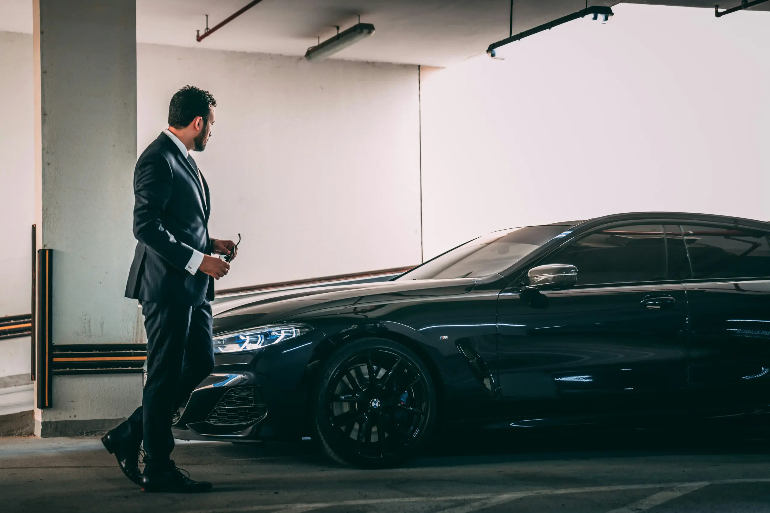 professional chauffeur in dark tailored suit standing beside polished black executive SUV at Sea-Tac airport arrivals with illuminated terminal signage