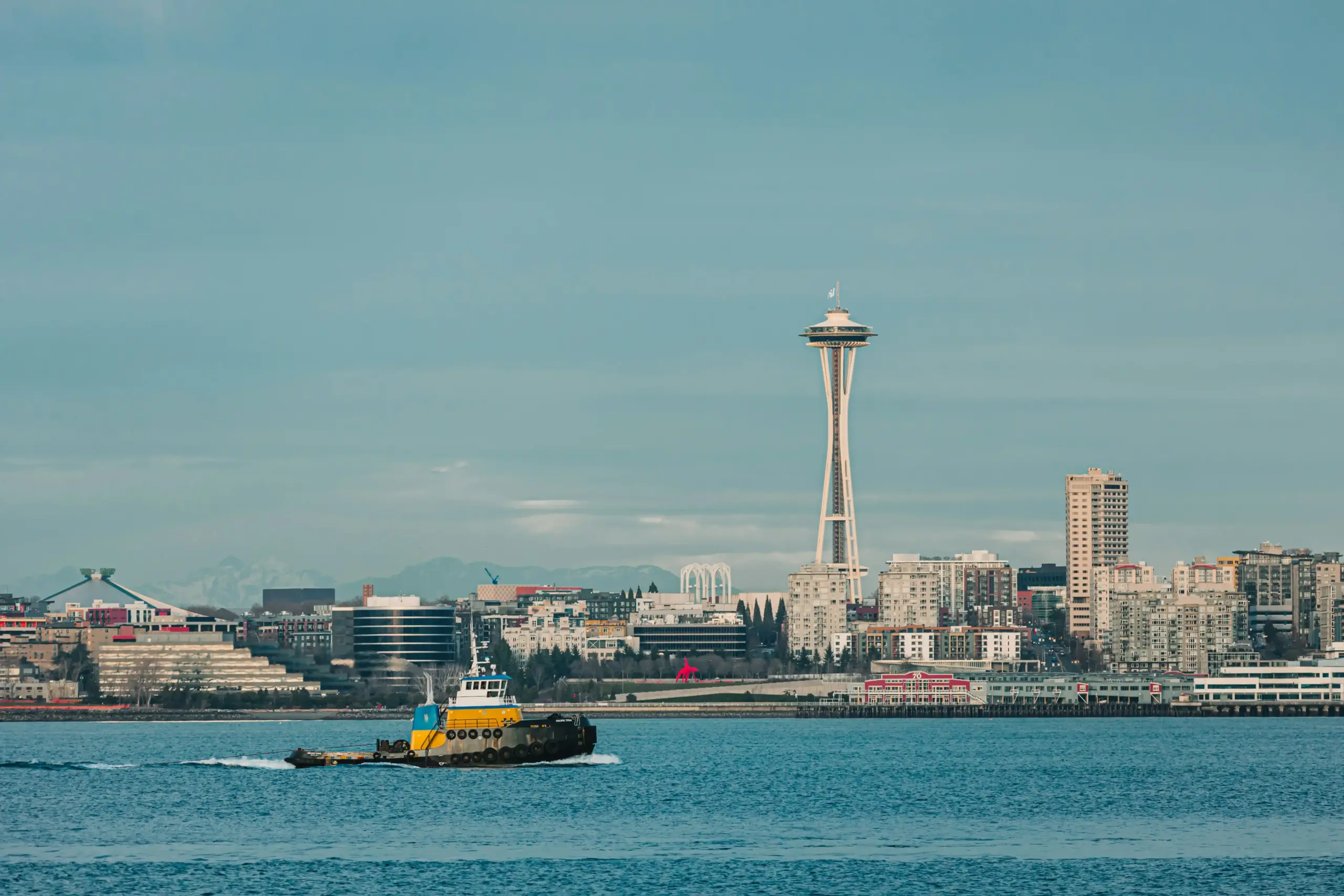 upscale black town car driving along Alki Beach at sunset with Seattle skyline across Elliott Bay, golden light reflecting on glossy paint