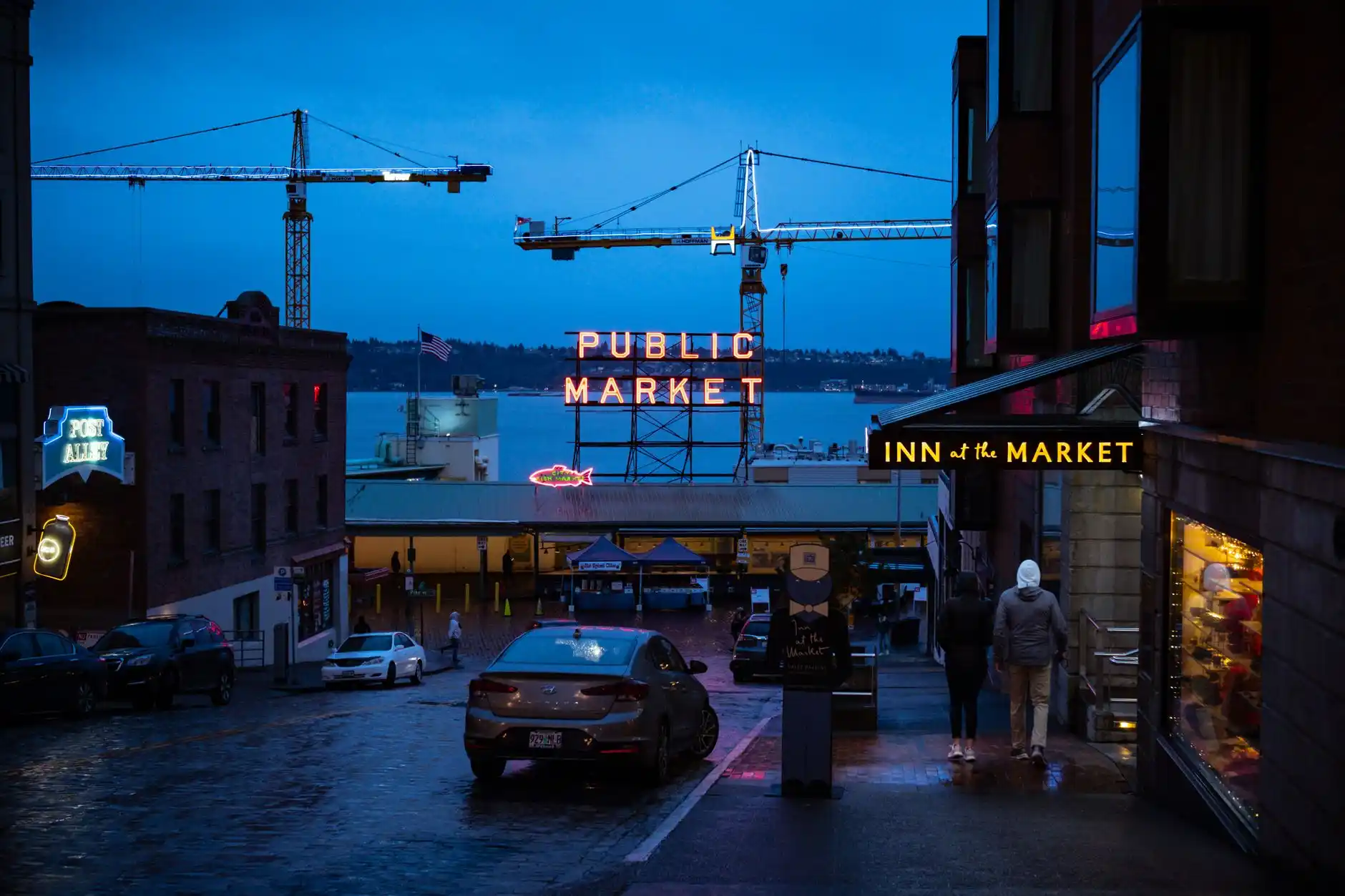 side-by-side visual of a polished black luxury town car and an older city taxi parked near Pike Place Market, overcast Seattle afternoon, clear contrast in vehicle condition