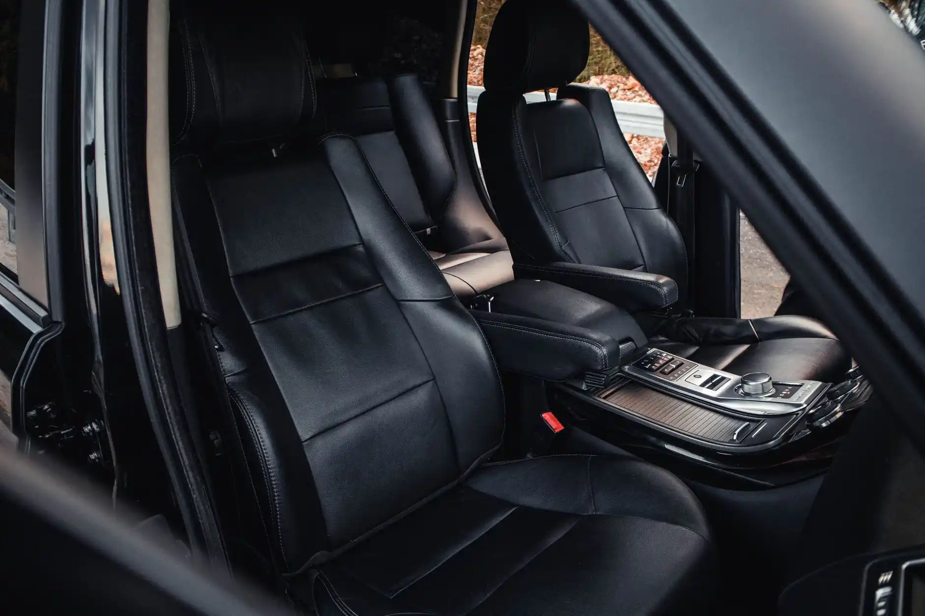 close-up luxury SUV interior comparison showing quilted leather captain seats, wood trim, panoramic dashboard lighting, and rain-speckled Seattle skyline through tinted windows