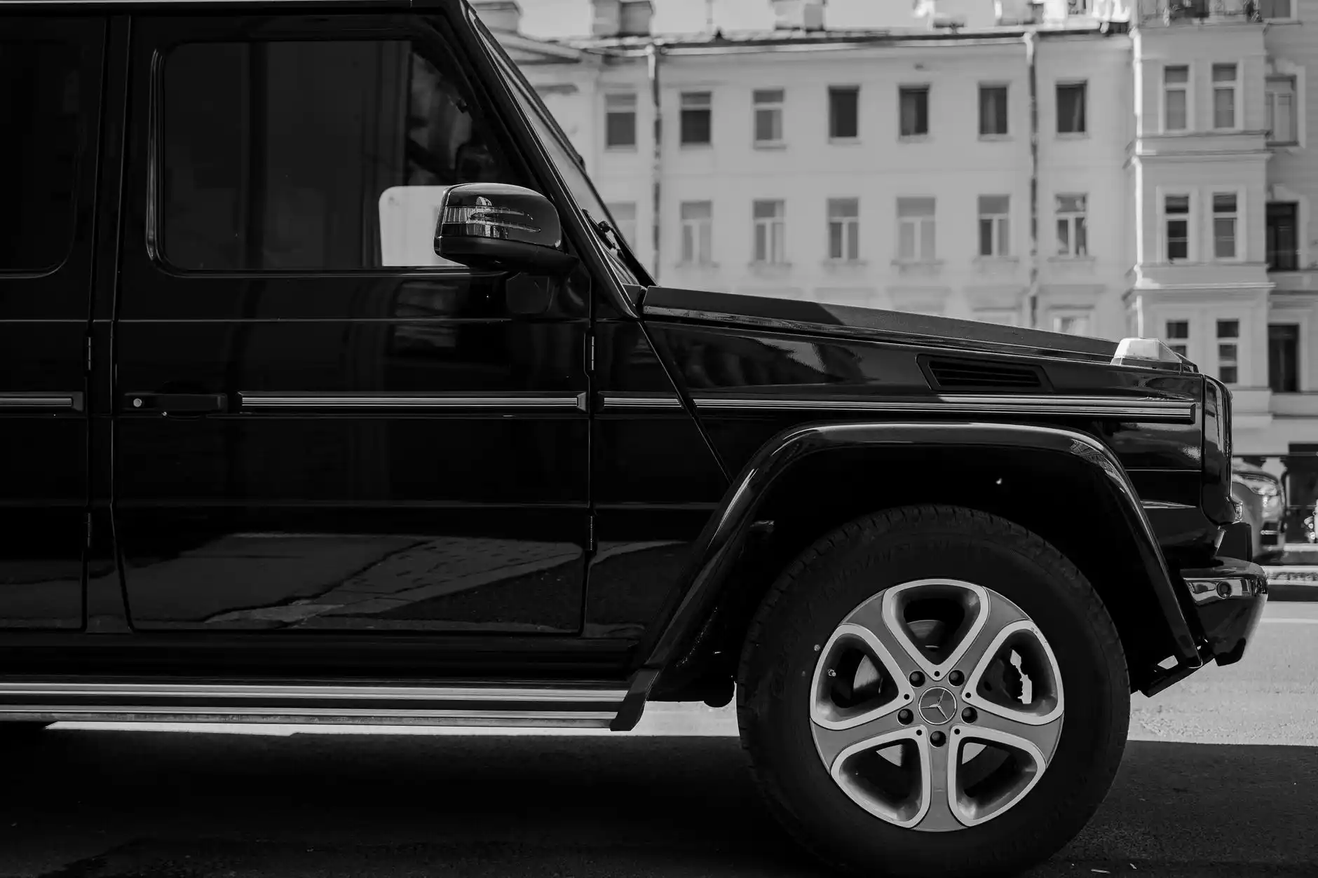 black luxury SUV curbside at Seattle-Tacoma International Airport during light rain, chauffeur opening rear passenger door, modern terminal glass reflecting city lights and wet ...