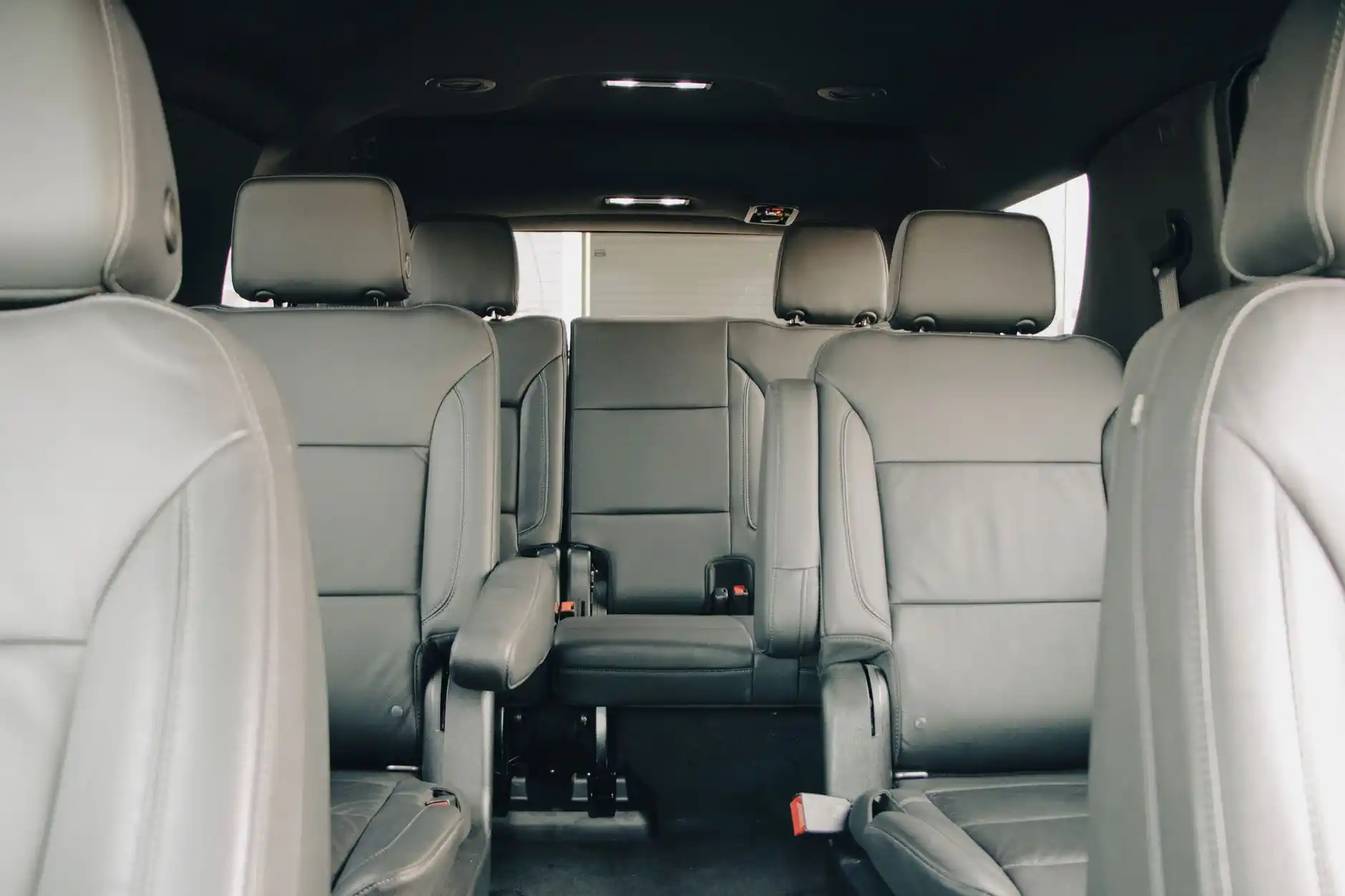 spacious luxury SUV interior with black leather captain seats, rear climate controls, bottled water, charging ports, and soft ambient lighting during a daytime city transfer
