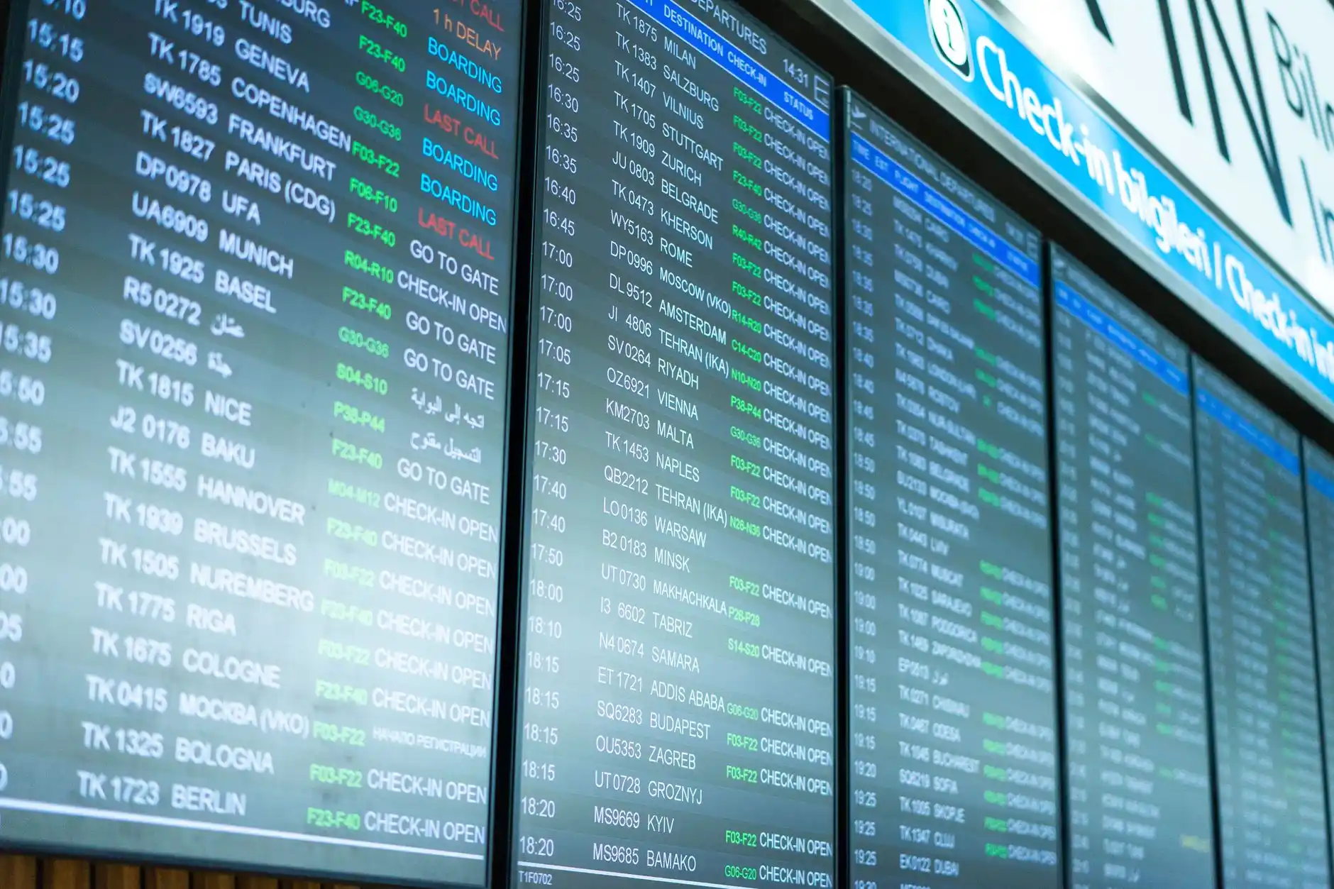 overhead view of SeaTac terminal drop-off lanes during light rain, black executive sedans moving efficiently, digital flight board visible through glass, travelers with carry-on...