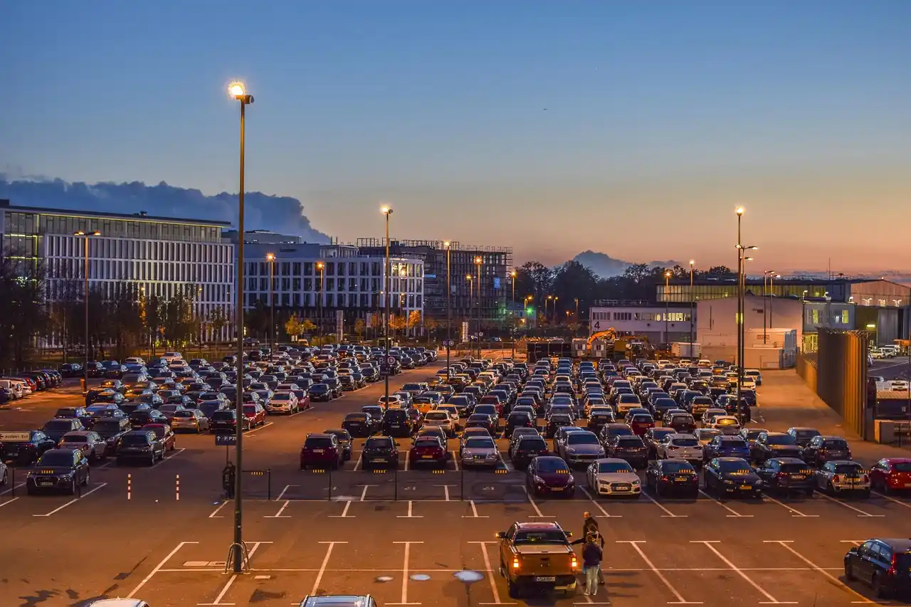 aerial view of crowded SeaTac airport parking garage with long rows of cars, travelers crossing lanes with suitcases, overcast Seattle sky, contrasted with a waiting black town ...