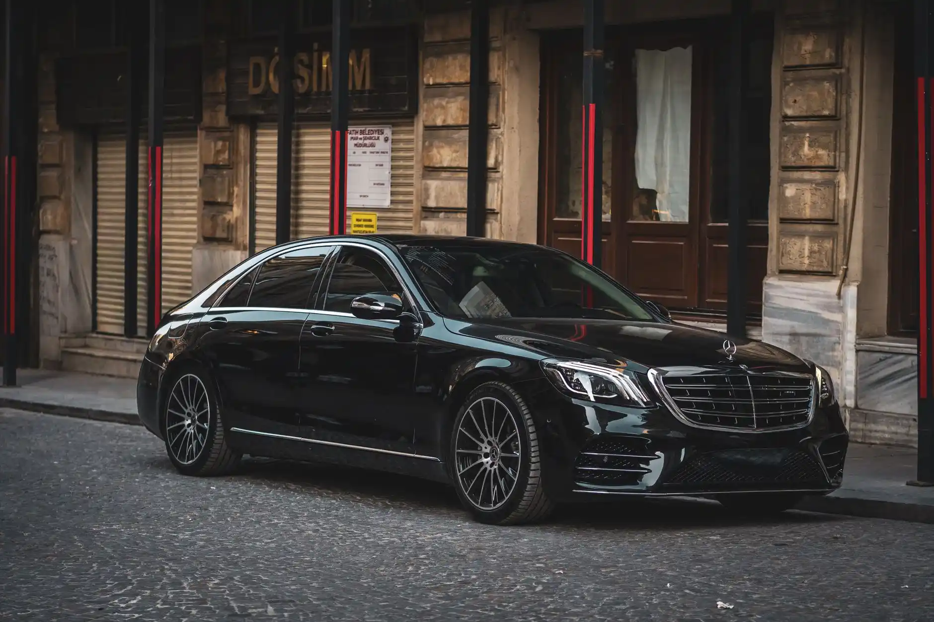 black luxury sedan and stretch limousine parked at Seattle-Tacoma airport curbside on a rainy evening, glowing terminal lights reflecting on wet pavement, professional chauffeur...