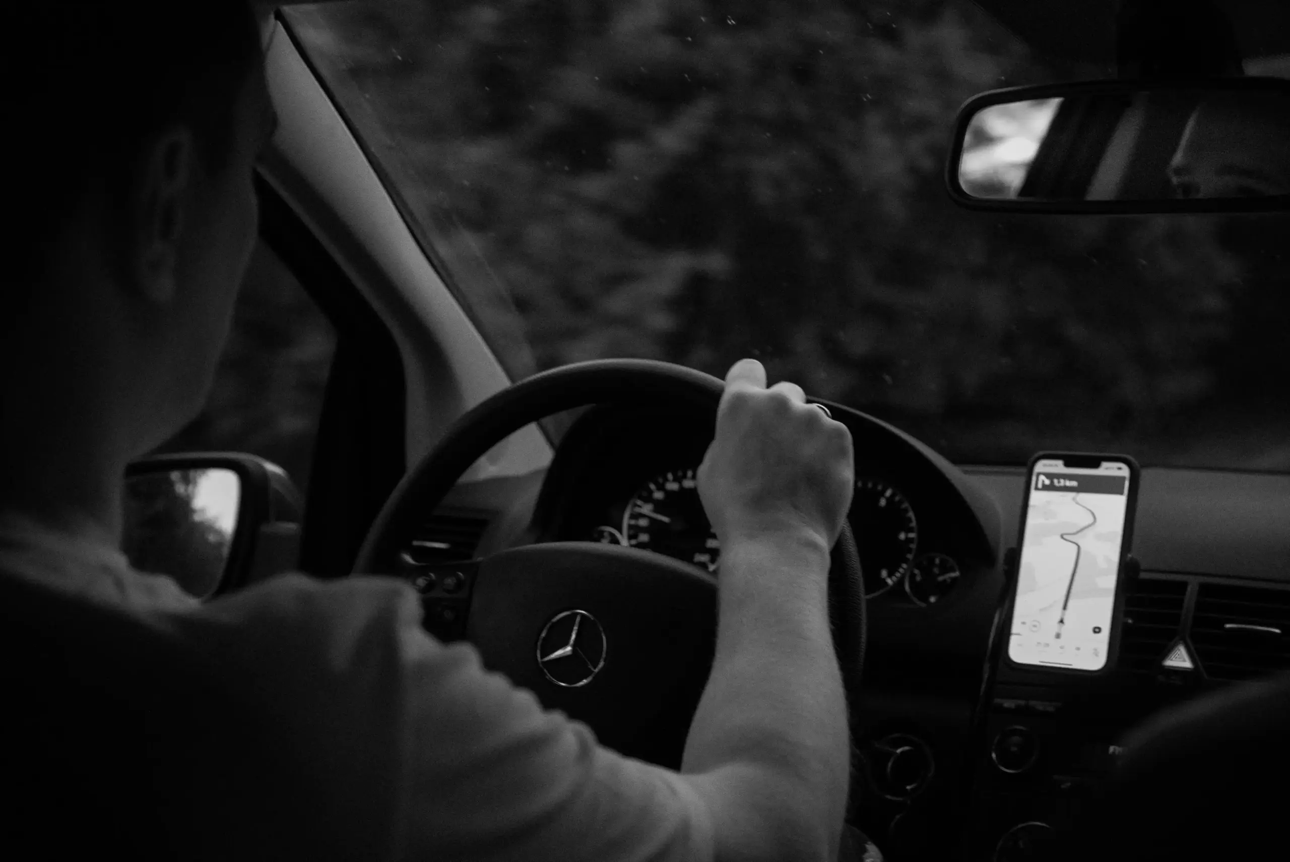 professional chauffeur in dark suit checking route on smartphone beside a polished black SUV in downtown Seattle, Space Needle faintly visible in background at dusk