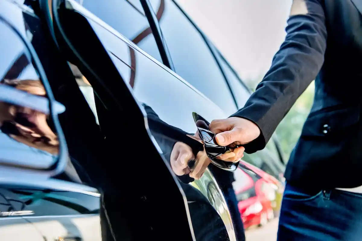 discreet chauffeur in a dark suit standing beside a polished luxury SUV outside a private aviation terminal near Seattle, soft overcast sky, minimal branding, elegant and secure...
