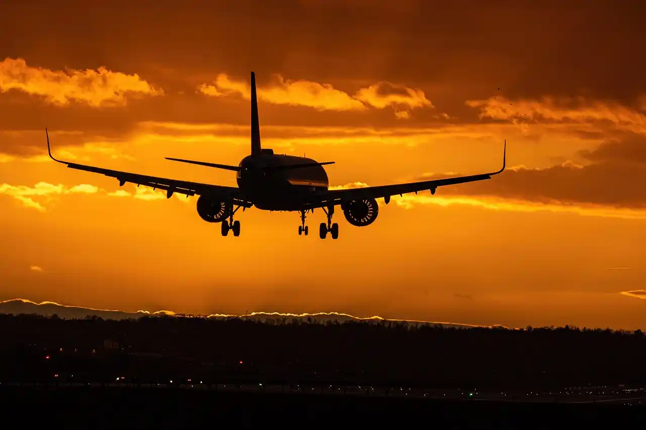 luxury SUV parked at Sea-Tac airport arrivals curb at dusk, chauffeur loading premium luggage while a well-dressed executive couple exits the terminal, glowing airport signage a...