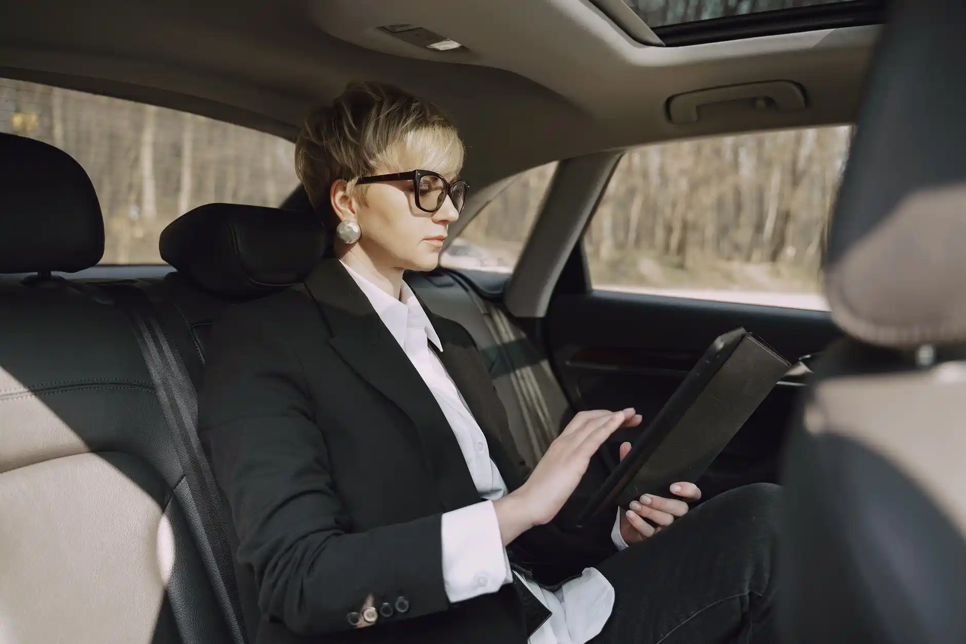 executive passenger seated in rear of luxury SUV using a tablet during transit through downtown Seattle, rain-speckled windows, soft leather interior, laptop bag and coffee neat...