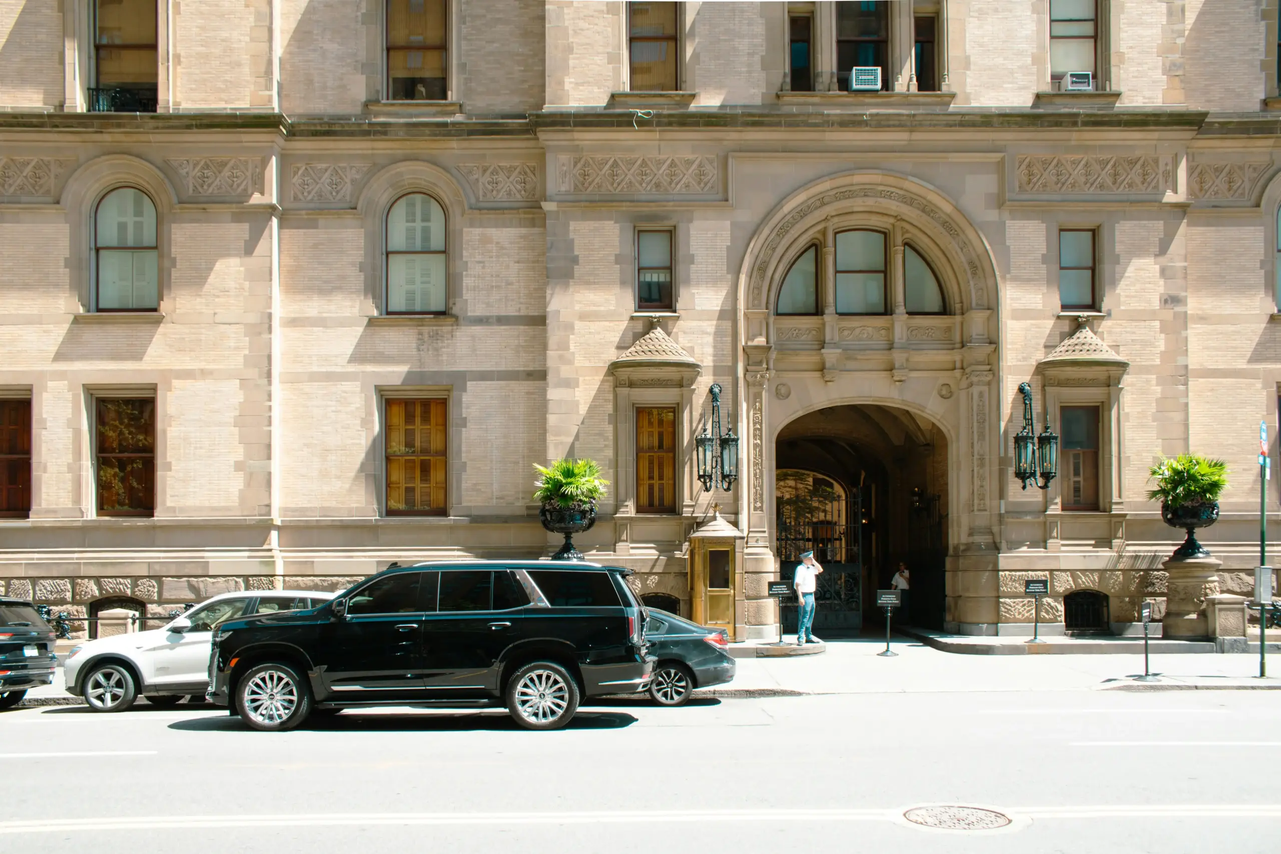 black stretch limousine and executive SUV parked curbside with chauffeur holding door, daylight city hotel entrance, realistic luxury transportation pricing concept