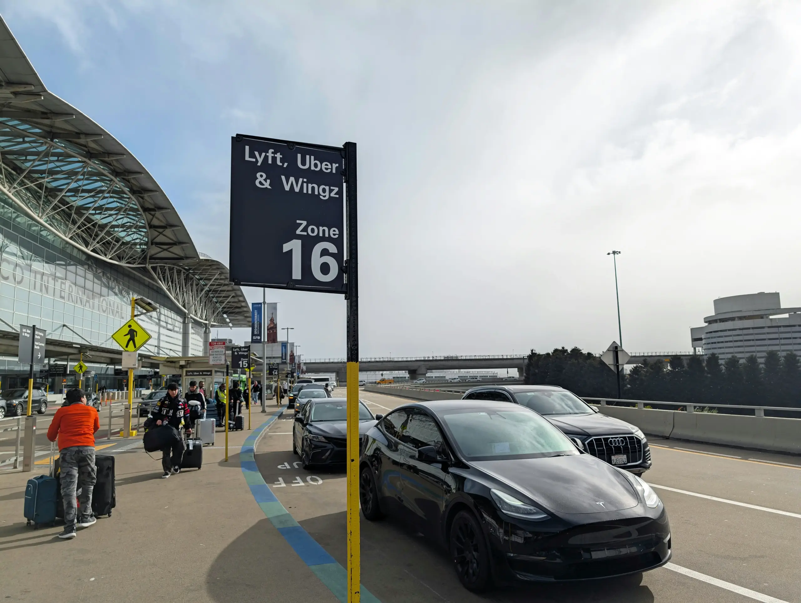 professional chauffeur in dark suit holding a name sign inside Sea-Tac arrivals area, polished black sedan waiting outside in covered pickup lane, travelers moving in background