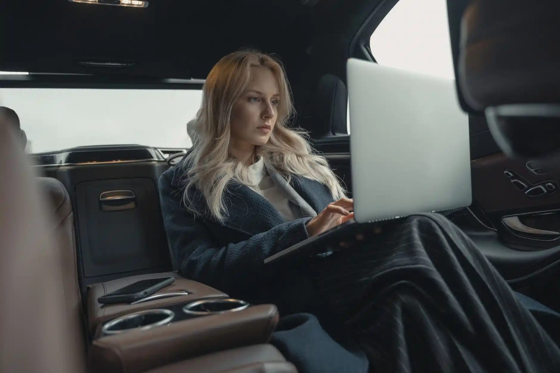business executive working on laptop in rear seat of luxury sedan while crossing downtown Seattle, rainy evening streets, soft city lights and Space Needle faintly visible