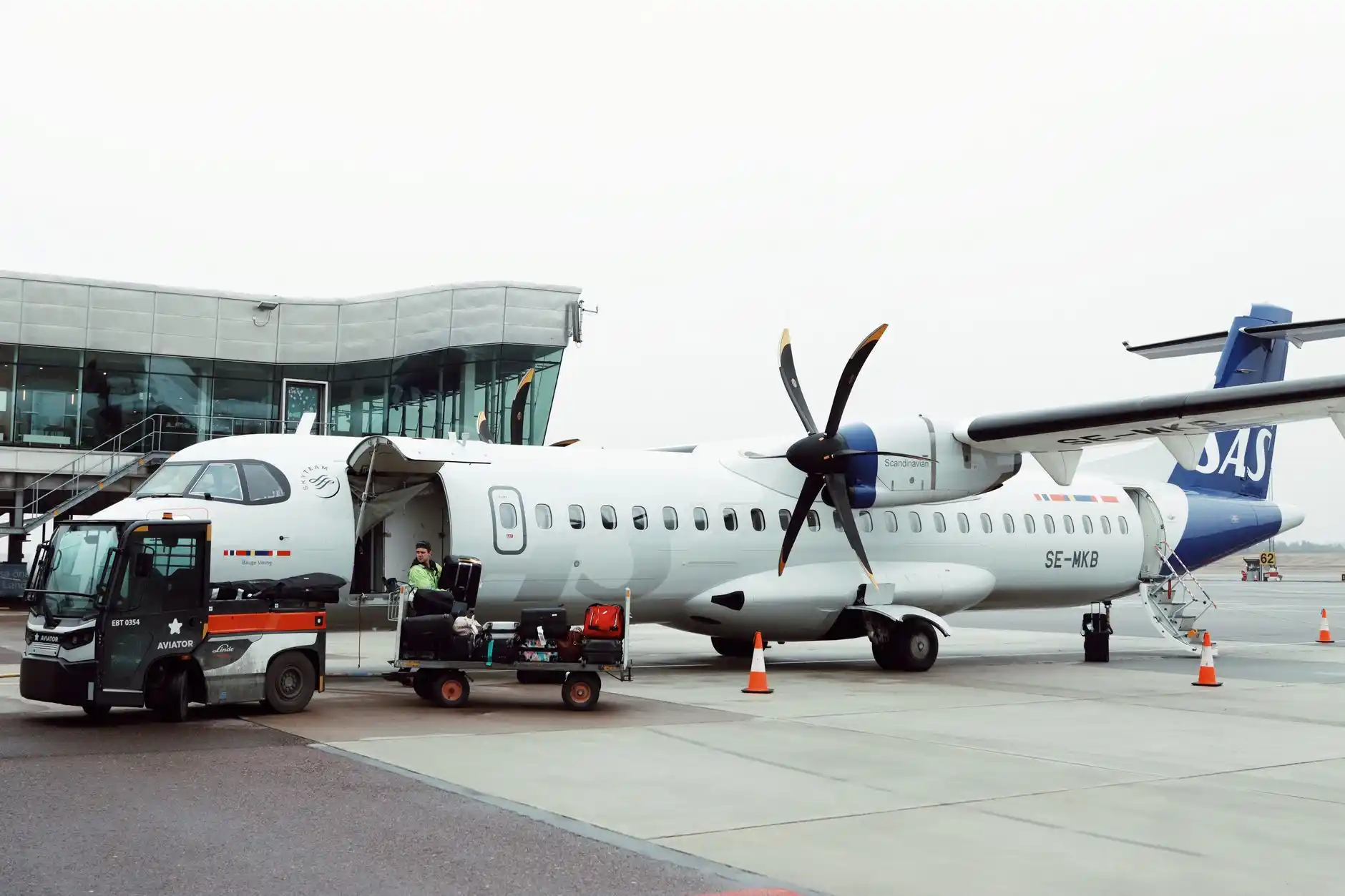Black private airport shuttle parked beside the Anacortes waterfront at sunrise, with rolling suitcases being loaded and the San Juan Islands visible in the distance