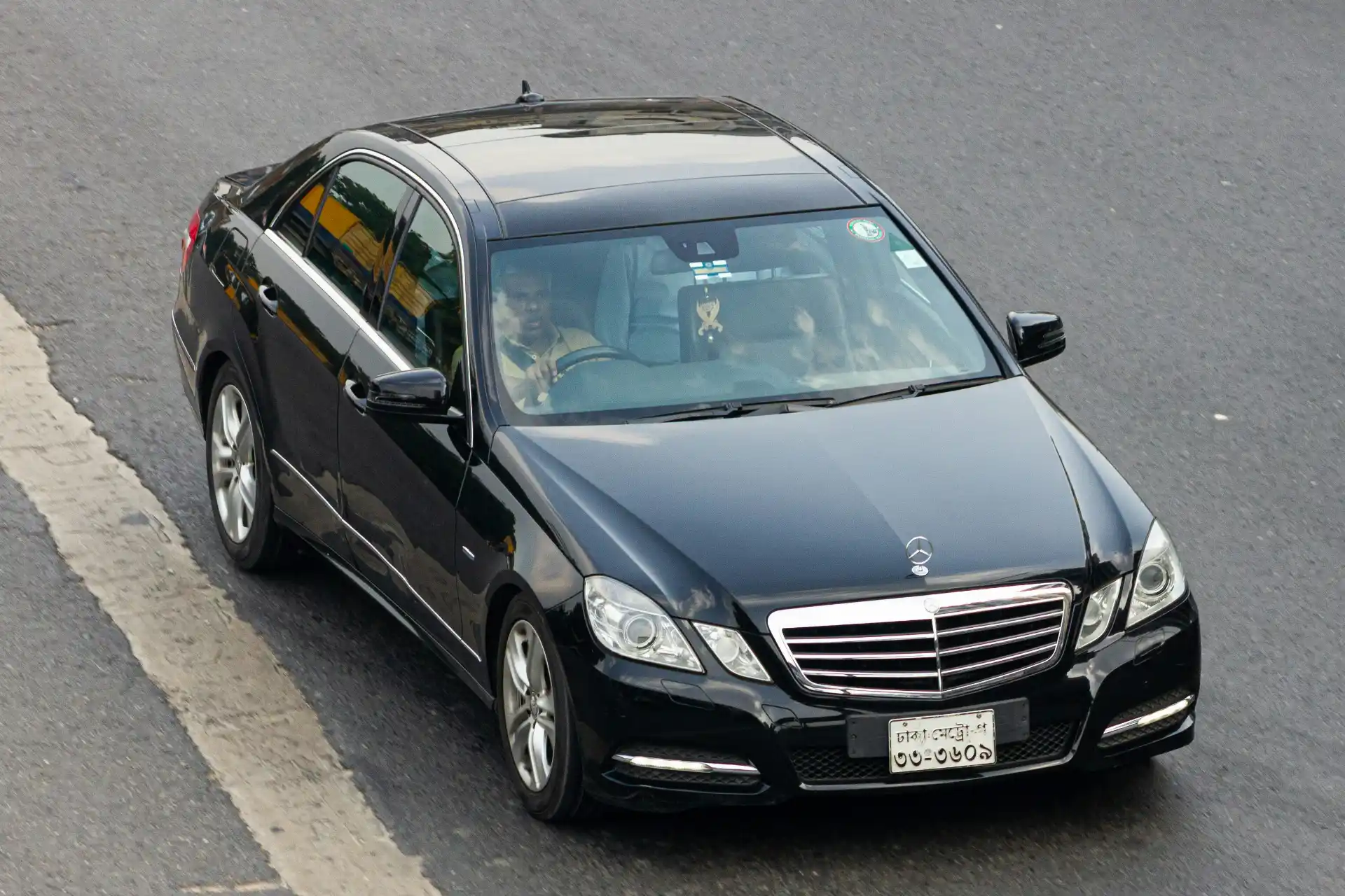Black luxury sedan with a professionally dressed chauffeur waiting beside the rear passenger door outside Paine Field terminal in Everett, Washington, overcast daylight